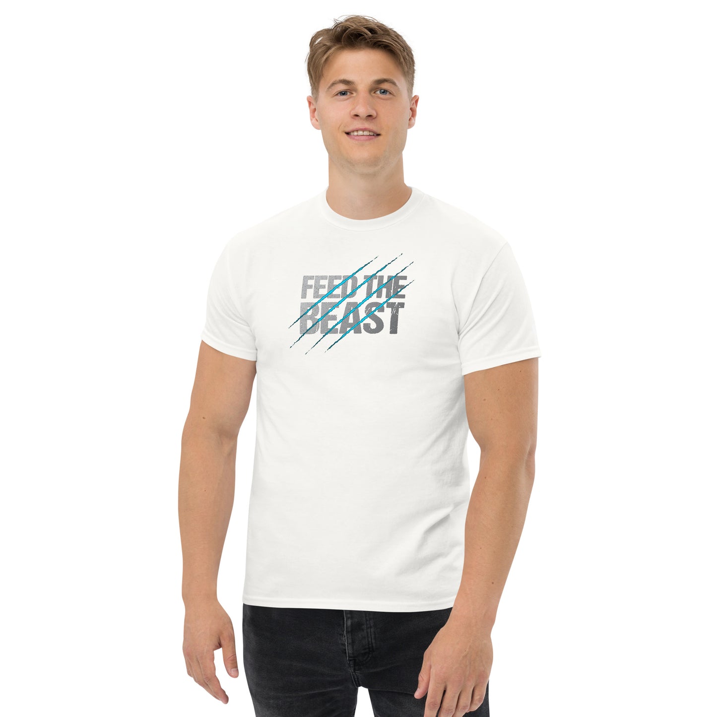 A young man with short blond hair, smiling gently and standing confidently. He is wearing a white t-shirt adorned with the words 'FEED THE BEAST' in blue and white text, accented with diagonal blue scratch marks. He pairs the t-shirt with dark jeans.