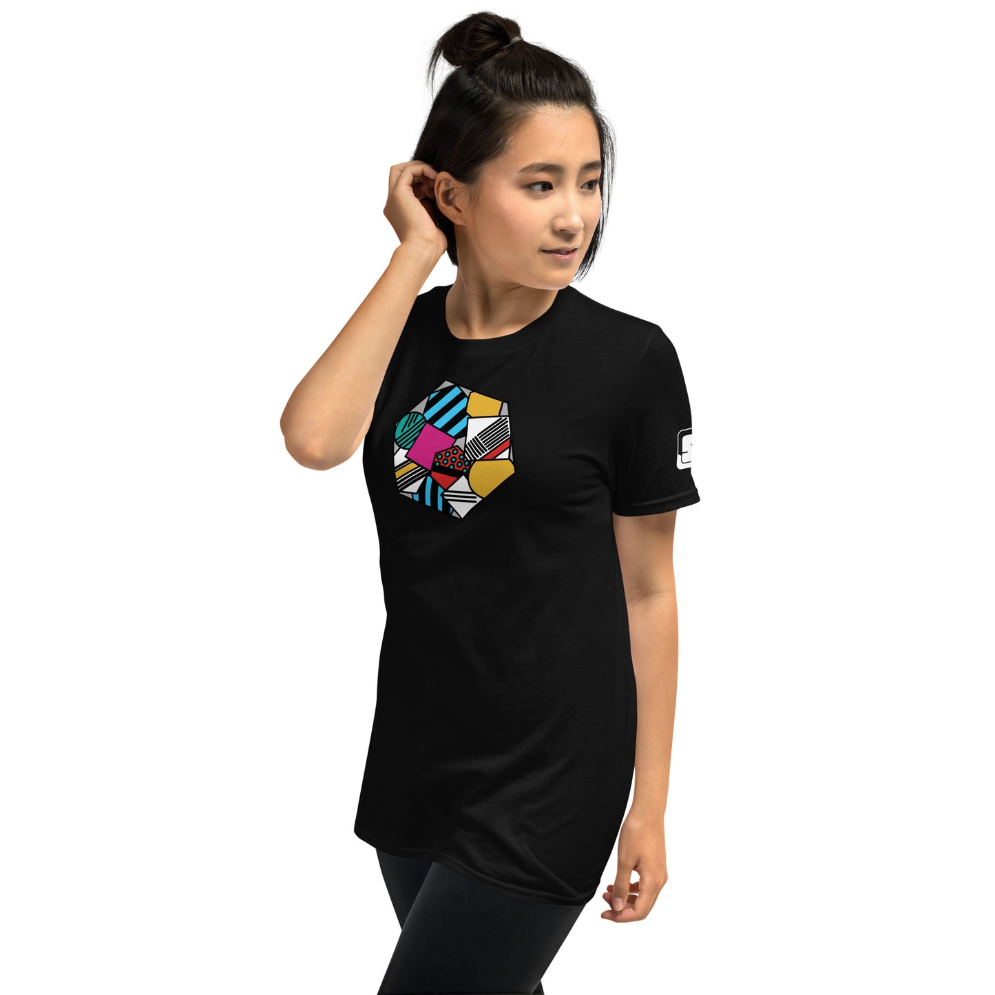 A young Asian woman models a sleek black tee featuring a vibrant, geometric patterned design in a hexagon shape. The design combines stripes, dots, and various textures in shades of blue, pink, yellow, and green.