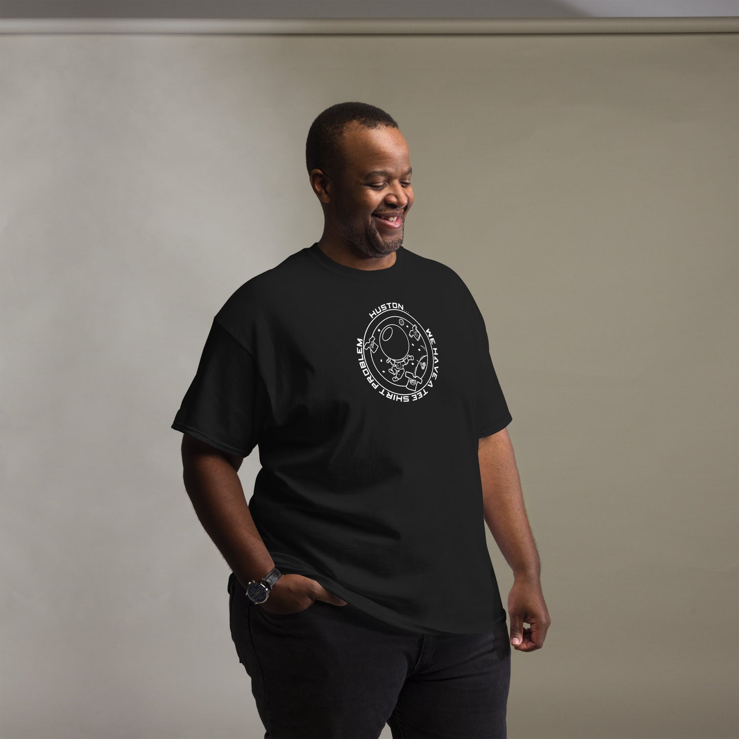 Man smiling in a black t-shirt detailed with a white "Houston...we have a tee shirt problem" graphic, depicting an astronaut amidst playful space-themed illustrations.