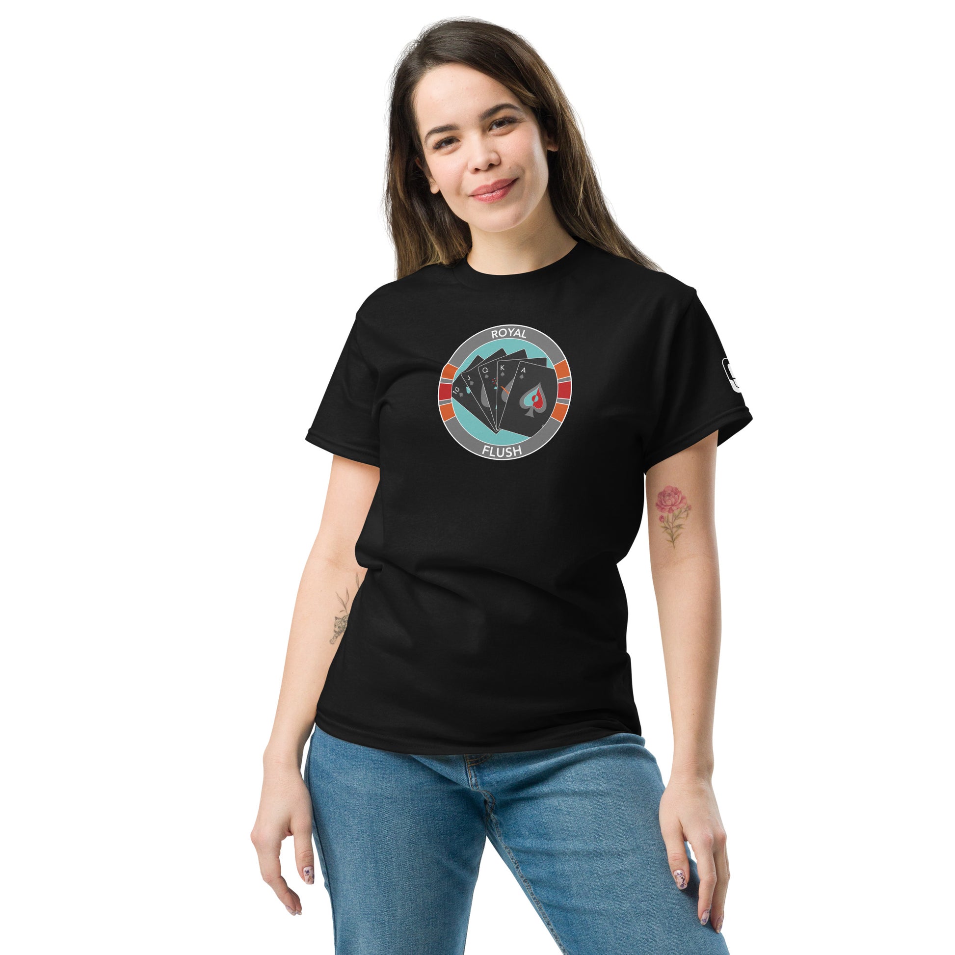 A young Caucasian woman models a black t-shirt featuring a centered graphic design of a royal flush poker hand within a poker chip, highlighted by sections of red and gray. The text "Royal Flush" circles the top of the design. She stands confidently, hands on hips, with a slight smile, wearing jeans and the t-shirt which fits comfortably, conveying a casual and stylish look.