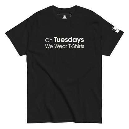 A black t-shirt displayed flat, featuring the phrase "On Tuesdays We Wear T-Shirts" in white uppercase letters across the chest. The shirt has a classic cut with a crew neck and short sleeves. A small logo patch is visible on the left sleeve, adding a subtle detail to the overall simple and modern design.