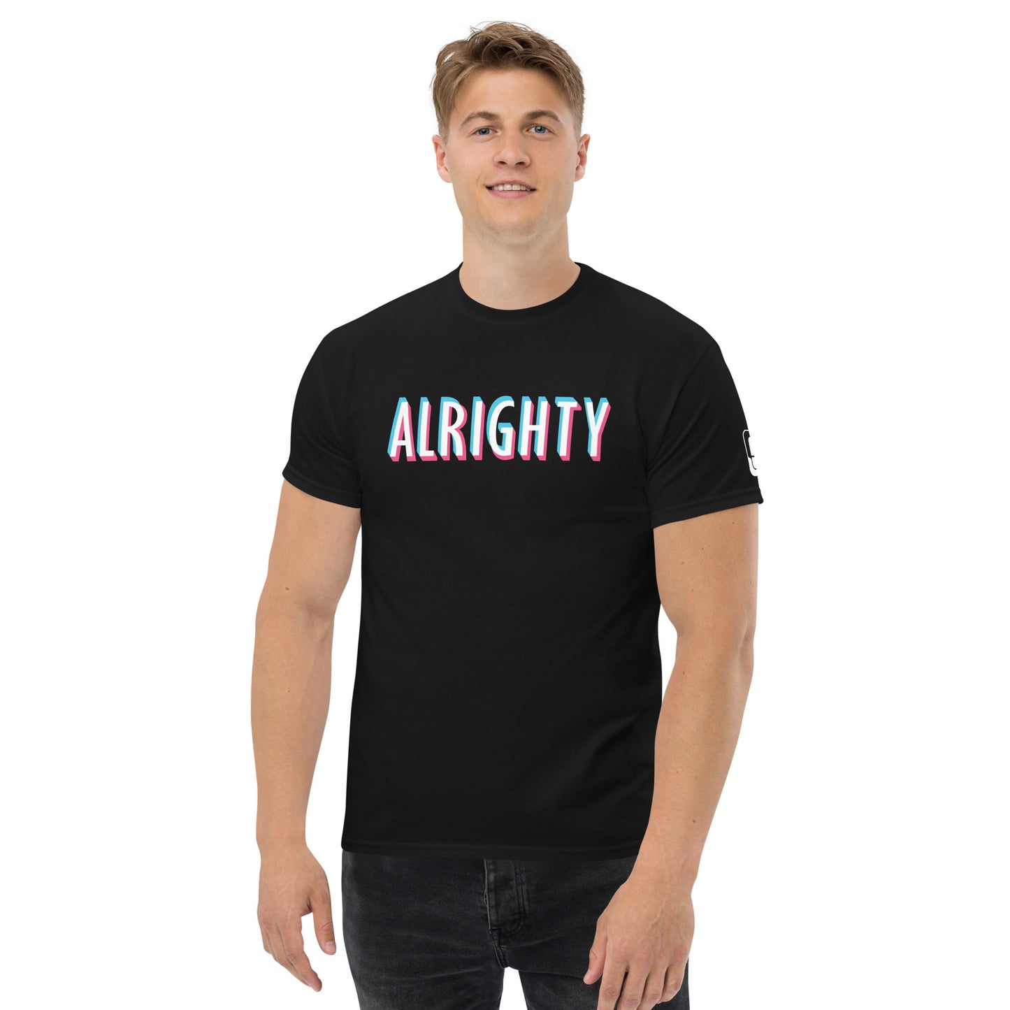 A young man with short blond hair stands confidently in a sleek black t-shirt featuring the word "ALRIGHTY" in a striking 3D-style font with a gradient of pink to light blue colors. His casual pose, with a slight smile and direct gaze towards the camera, complements the simple yet bold design on the shirt. The background is plain, focusing attention on the vivid text and his relaxed demeanor. He pairs the t-shirt with dark jeans for a modern, stylish look.