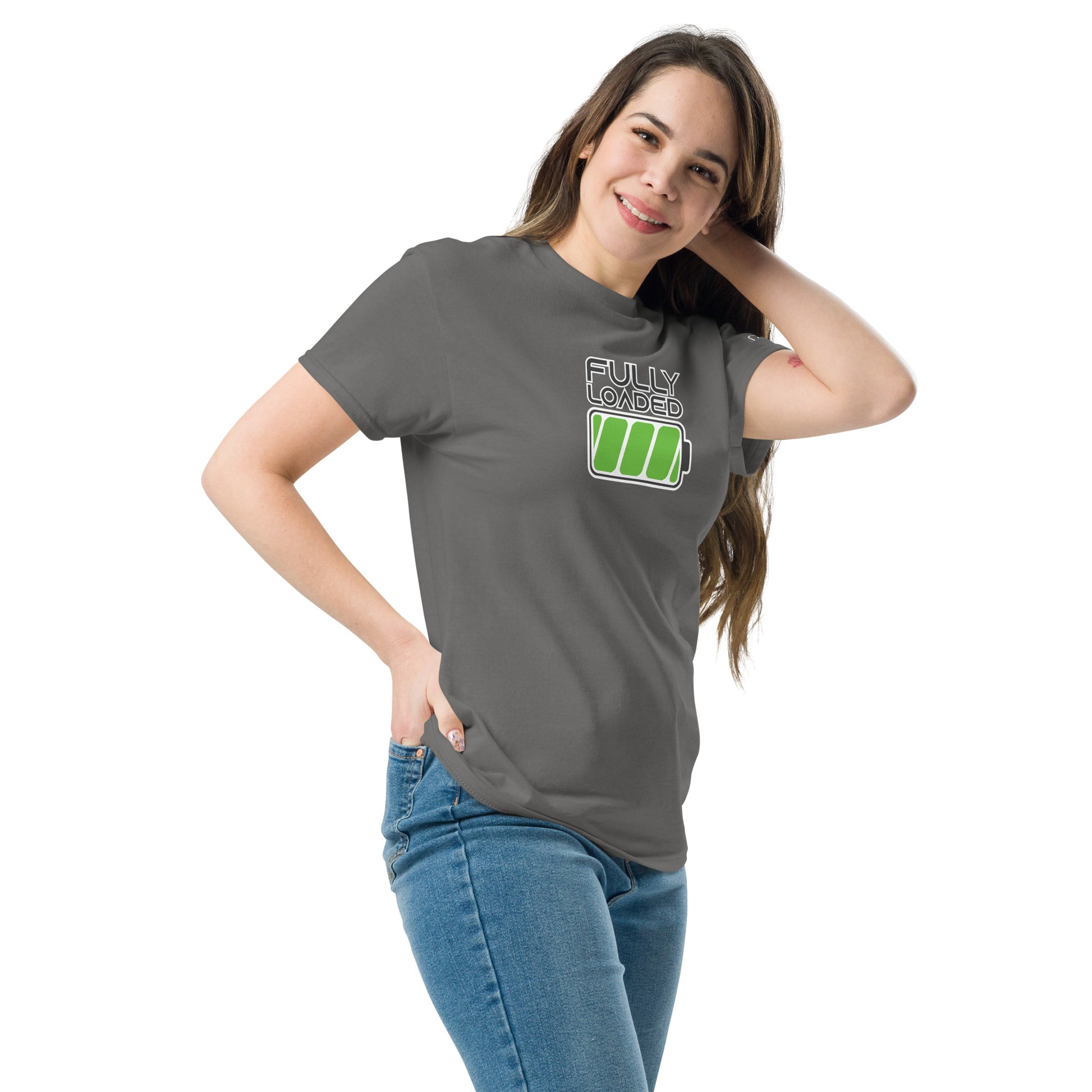 A young Caucasian woman poses playfully in a fitted gray t-shirt that displays a vibrant green battery icon graphic with the words "FULLY LOADED" above it in bold, white lettering. She stands relaxed with her left hand on her hip and her right hand gently resting on her head, wearing a slight smile. The t-shirt pairs casually with blue jeans, enhancing a comfortable yet stylish appearance.