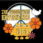 A vibrant and nostalgic graphic representing "The Woodstock Experience 1969". This design features bold, retro-style lettering atop a stylized peace symbol background framed by a circular border. Orange and pink flowers, indicative of the 1960s counterculture and peace movements, adorn the bottom. A simple white dove perches on the upper right, symbolizing peace. The overall composition captures the essence of the iconic Woodstock music festival, emphasizing peace, music, and the free-spirited vibe of the e