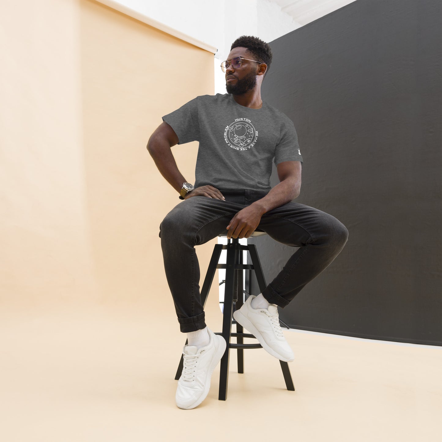 Man modeling a dark heather t-shirt that reads "Houston...we have a tee shirt problem" in a white circular graphic. The design includes a stylized astronaut, planets, and whimsical space elements