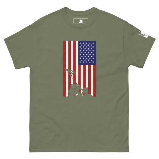 A military green T-shirt displays a vertically aligned American flag, with a blue square full of stars in the upper left and stripes of red and white extending downwards. At the base of the flag, there's a silhouette of the iconic Iwo Jima flag-raising scene, depicting soldiers working together to hoist the flag. This graphic blends historical reverence with a modern style on the T-shirt.