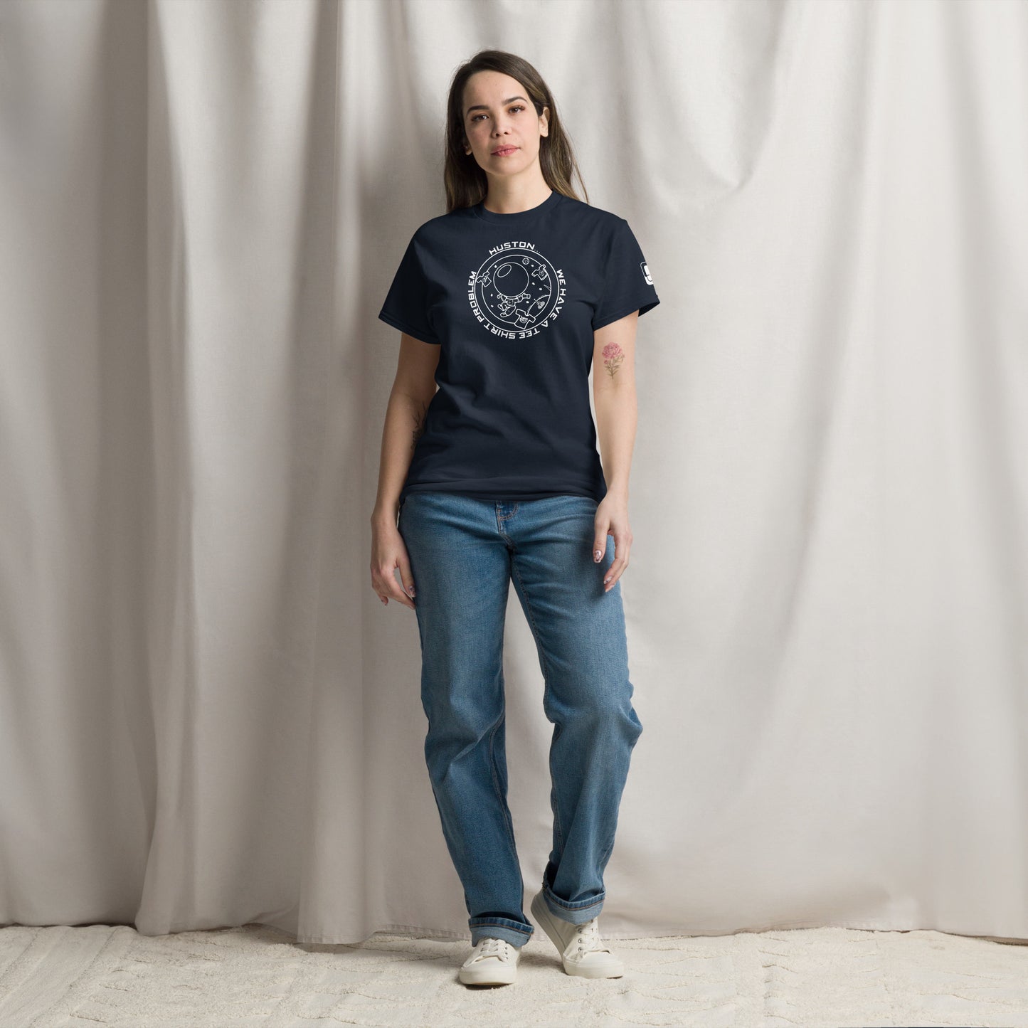 Woman casually posing in a navy t-shirt that features a white graphic saying "Houston...we have a tee shirt problem," with elements like an astronaut and stars drawn in a fun style.