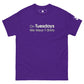 A vivid purple t-shirt displayed flat with the playful phrase "On Tuesdays We Wear T-Shirts" printed in white uppercase letters across the chest. The shirt has a classic crew neckline and short sleeves, featuring a small logo patch on the left sleeve, adding a subtle branded touch to the simple yet statement-making design.