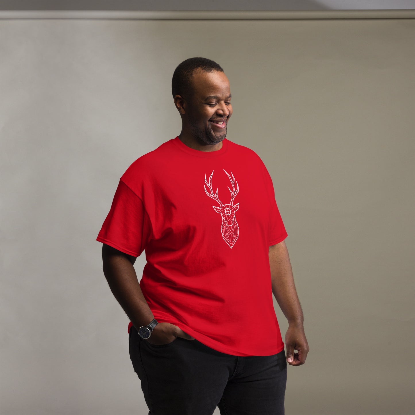 A smiling African American man wearing a casual red t-shirt with a minimalist white deer head design on the front, standing in a studio setting.