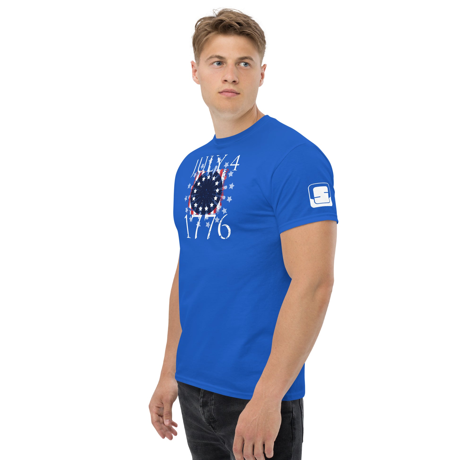 A young Caucasian man models a vibrant royal blue t-shirt emblazoned with the "July 4, 1776" design in white, also featuring stars and stripes. His pose is upright and confident, with a soft gaze looking off-camera, conveying a casual yet attentive demeanor. The shirt's bright color and patriotic motif make it an ideal choice for Independence Day celebrations or any casual setting that calls for a touch of American pride.