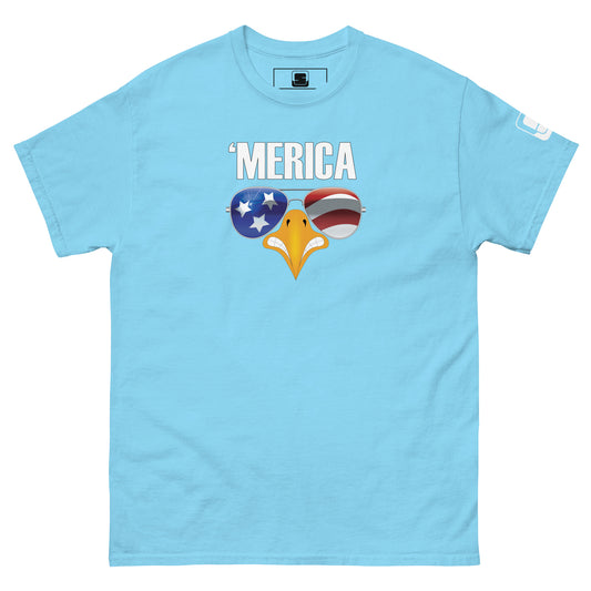 A light blue t-shirt displayed flat, adorned with a humorous and patriotic graphic. The shirt features the phrase "'MERICA" in large, uppercase letters, with a stylized eagle's beak depicted below it. The beak is designed with aviator sunglasses that reflect American symbolism: the left lens has a blue background with white stars, and the right lens showcases red and white stripes, mimicking the American flag. This spirited design emphasizes American pride in a lighthearted manner.