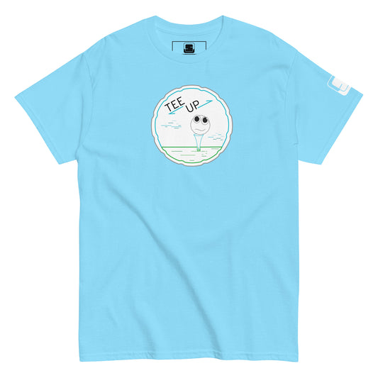 A light blue t-shirt displayed flat, featuring a playful golf-themed graphic centered on the chest. The graphic includes a cheerful golf ball character perched on a tee, encircled by a light blue outline resembling a golf hole. Above the golf ball, the phrase "TEE UP" is displayed in fun, casual lettering, adding a spirited touch to the shirt. This t-shirt combines casual sportiness with a quirky design, making it an appealing choice for golf fans and those enjoying a lighthearted style.