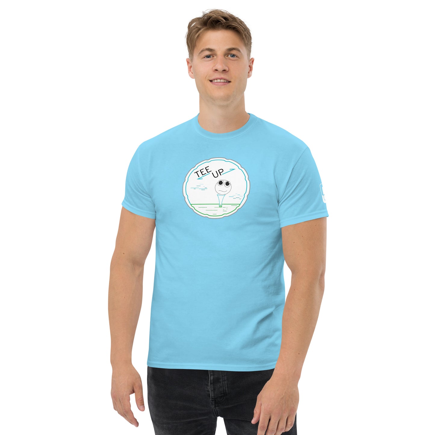 A man stands confidently wearing a light blue t-shirt that showcases a charming golf-themed graphic. The design, centered on the chest, features a golf ball with a face, perched on a tee within a circular outline marked by the phrase "TEE UP" in a playful, modern font. The shirt's vivid color complements the simple yet appealing white and green of the graphic, lending a fresh and casual look perfect for a small gathering.