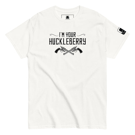 The image features a plain white t-shirt with a black graphic print. The print says "I'm Your Huckleberry" in a western-style font, accented by two crossed revolvers beneath the text. The design evokes a classic Western movie feel, suitable for fans of old Westerns or iconic movie lines. The t-shirt also shows a small logo patch on the sleeve, adding a subtle detail to the casual design.