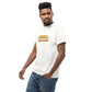 Stylish young man in a casual pose wearing a white t-shirt with a playful sandwich graphic  featuring the text 'FEED THE BEAST' as the deli meat inside the bun. He sports a trendy hairstyle and a confident smile, looking to his left. His relaxed stance and the plain background emphasize the fun and youthful design of the shirt.