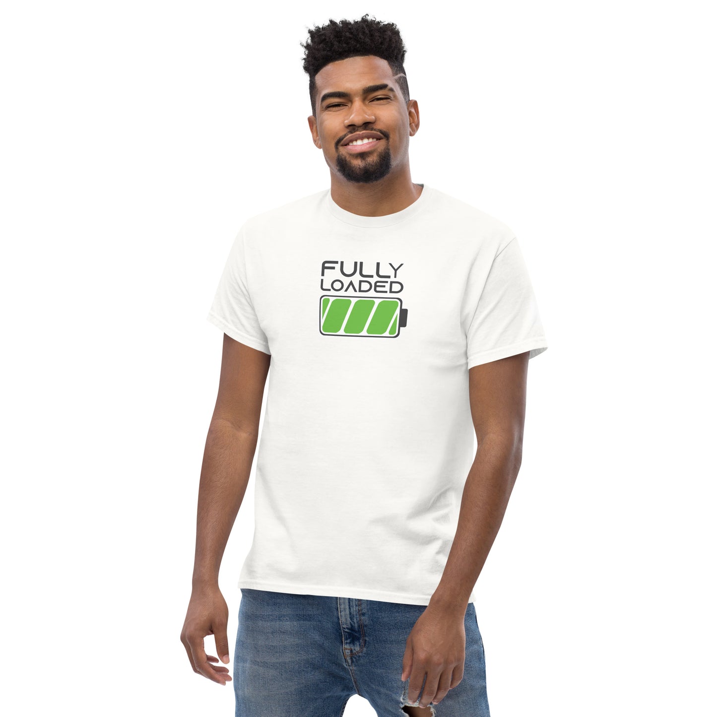 
A young African American man with a confident smile models a white t-shirt featuring a green battery icon and the words "FULLY LOADED" printed in black. He sports a stylish haircut and casual demeanor, standing with one hand slightly touching his jean pocket. The t-shirt's clean design and vibrant graphic make it pop against his casual blue jeans in a light, informal setting.