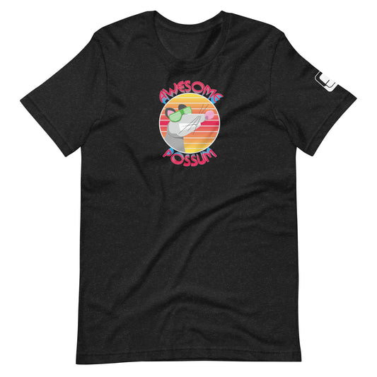 A heather black t-shirt featuring a vibrant graphic with the phrase "AWESOME POSSUM" encircling a cheerful possum character sporting green sunglasses. The possum is set against a multicolored circular background that mimics the hues of a sunset in shades of red, orange, and yellow, adding a lively and playful touch to the shirt's design.