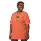 A joyful African American woman with a bright smile, wearing an orange colored t-shirt featuring a playful "Taco Tuesday" design. The shirt's graphic shows a cheerful fish in a taco, wearing a sombrero and giving a thumbs-up. Her relaxed and happy demeanor, paired with casual denim jeans, complements the light-hearted, festive theme of the shirt, making it a charming choice for casual wear or themed events.