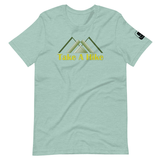 A pale green t-shirt displays a central graphic featuring stylized green mountain peaks with a yellow text below reading "Take A Hike." The shirt has a casual fit with short sleeves and a round neckline, and includes a small black logo patch on the right sleeve. The design is centered on the chest, making it a clear focal point for an outdoor-themed look.