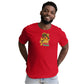 A cheerful young African American man with a bright smile, wearing a vibrant red t-shirt that features a whimsical "Taco Tuesday" graphic. The graphic depicts a happy fish in a taco, adorned with a colorful sombrero, making a thumbs-up gesture. The shirt's design is fun and playful, perfect for a casual day out or a themed event. The man's engaging expression and casual posture in light-wash denim jeans enhance the shirt's appeal, making it a joyful fashion statement.