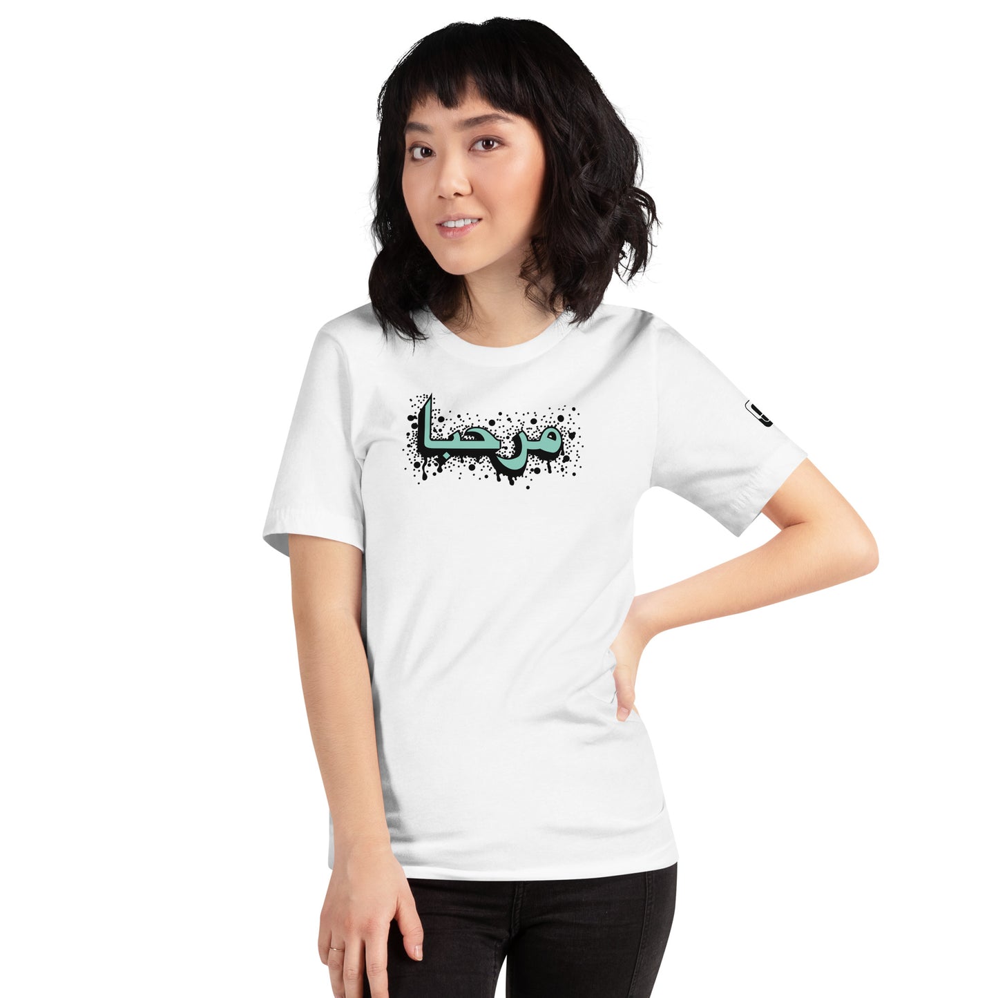 Confident woman with a bob haircut wearing a white t-shirt adorned with turquoise  Arabic calligraphy featuring black detailing, a small logo patch on the sleeve, and posing with one hand on her hip against a white background.