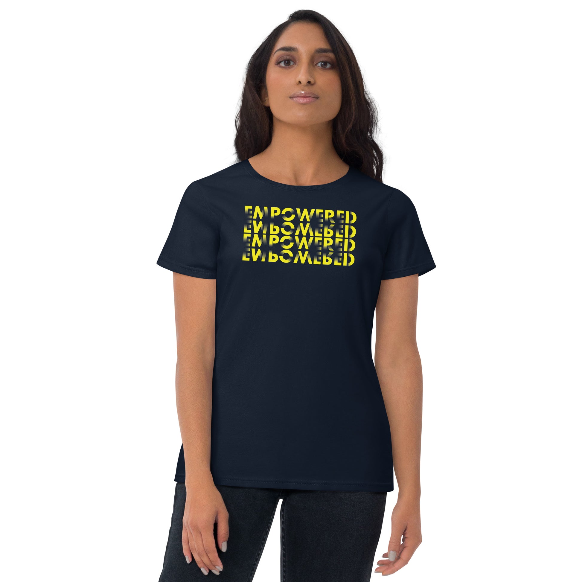 
A young South Asian woman stands with a serene expression, modeling a navy blue t-shirt that displays a creative text design. The shirt features the word "EMPOWERED" printed in yellow four times in a 3D cube illusion, creating an impactful visual on the dark fabric. Her posture is relaxed, with her arms gently at her sides, emphasizing the empowering theme of her attire.